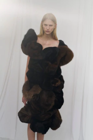 Model wearing a dark textured sculptural garment against a white draped background in an editorial photograph by Ola Rindal.