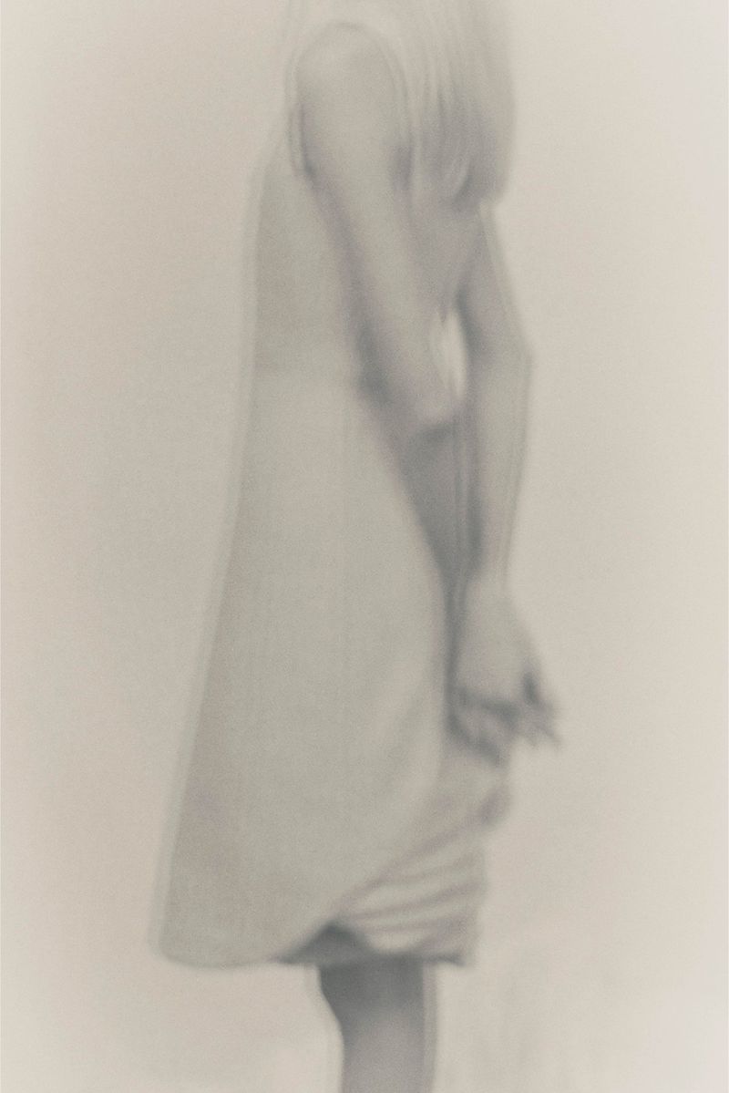 Blurred image of a person in a light-colored dress, creating a soft, ethereal, and dreamlike quality with a minimalist aesthetic.
