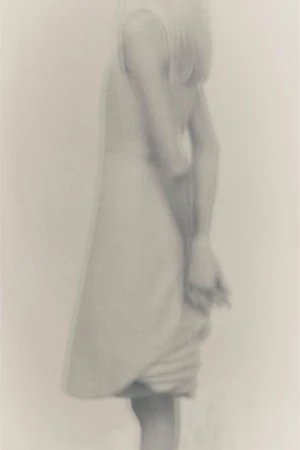 Blurred image of a person in a light-colored dress, creating a soft, ethereal, and dreamlike quality with a minimalist aesthetic.