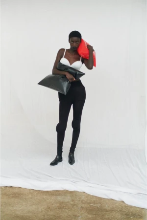 Model standing against a white backdrop holding large black cushions and a bright red object for the Crosscurrent Extension project.