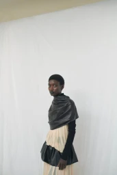 Model wearing a pleated dress and dark wrap against a plain white studio backdrop