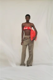 Model standing against a white seamless background wearing a red bandeau top and trousers, holding a bright red clutch bag.