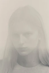 Close-up portrait of a model with long hair against a light neutral background captured with a soft double exposure effect.