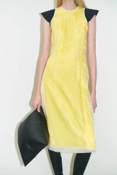 Model in yellow dress with black cap sleeves holding a dark pillow bag against a plain white background