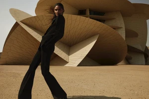 Model in a black suit standing in front of organic, disk-like architectural structures under clear sky