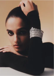 Close-up portrait of a woman wearing a wide diamond cuff bracelet on a black long-sleeve top against a warm beige background.