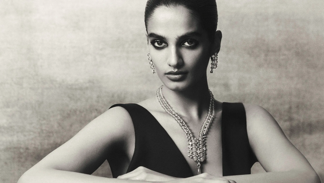 Black and white portrait of a woman wearing layered beaded necklaces and drop earrings against a textured background
