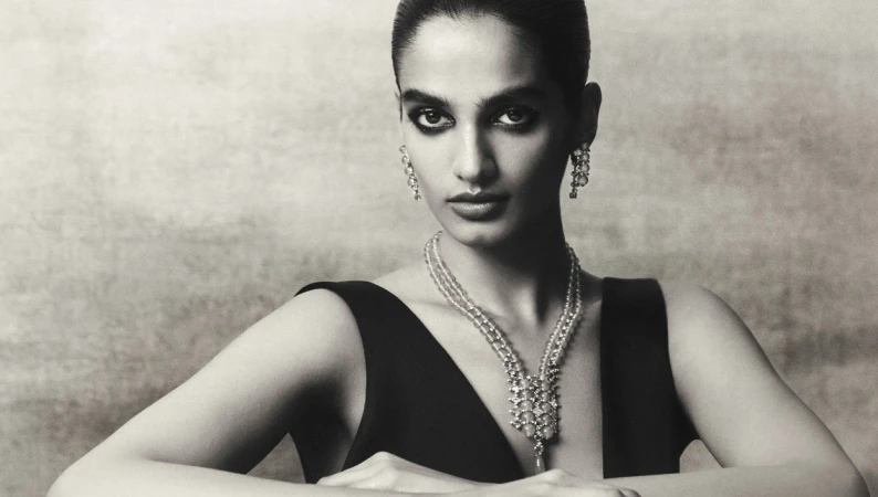 Black and white portrait of a woman wearing layered beaded necklaces and drop earrings against a textured background