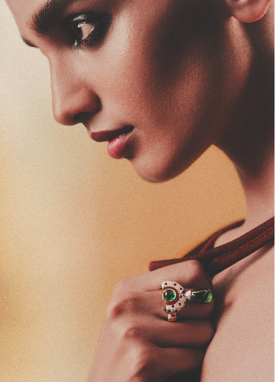 A woman's profile showcases a statement ring on her finger, close-up shot in a studio setting, against a soft yellow backdrop.