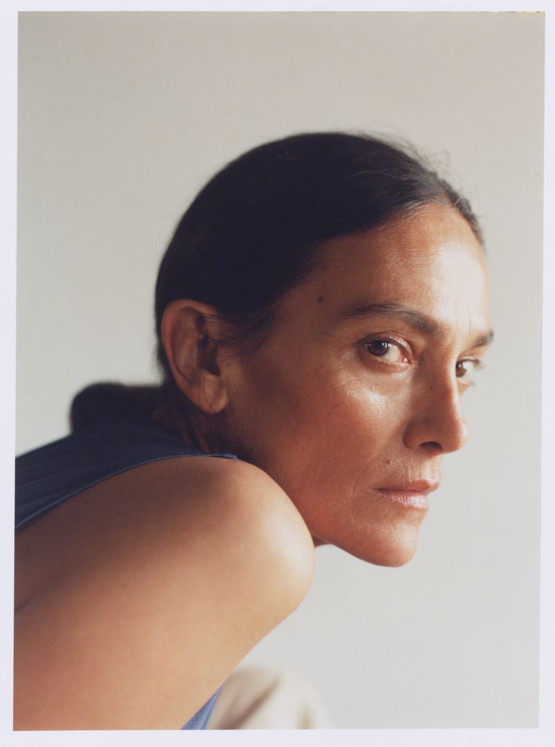 Close-up portrait of an adult woman looking over her shoulder in a photo studio with neutral tones and soft lighting.