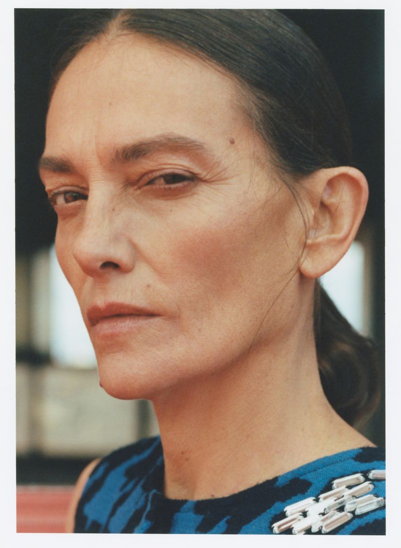 Headshot of a middle-aged woman with dark hair, wearing a blue and black patterned dress with jeweled embellishments, looking at the camera.