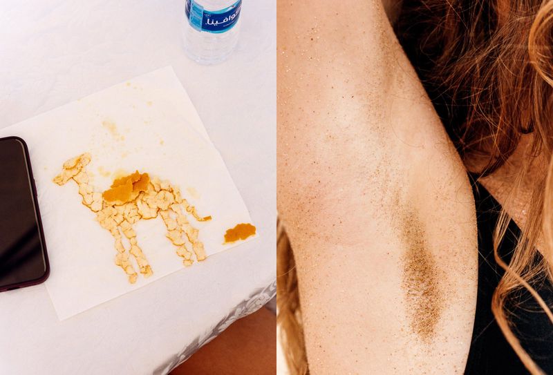 Armpit with hair contrasted against a drawing of a camel on a napkin next to a phone and bottle of water on a white surface.