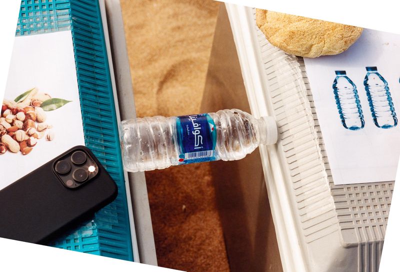 Still life featuring a water bottle, nuts, smartphone, and bread on a striped surface with a tan background.