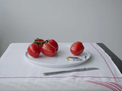 A white plate on a white cloth holds cluster tomatoes and a single unwrapped candy next to a knife.