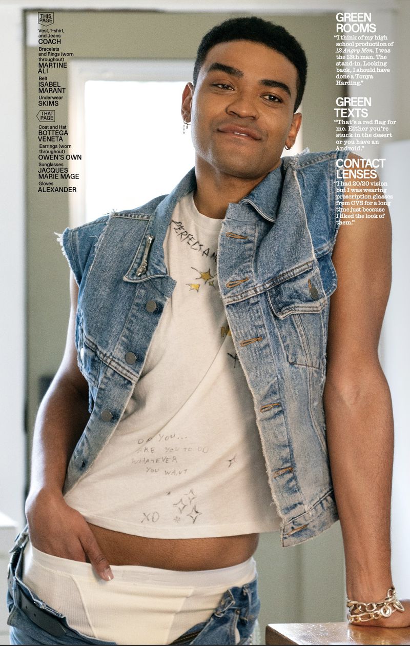 Stylish, youthful portrait of a mixed-race man indoors, wearing a denim vest and white graphic tee, showing off fashion-forward streetwear.