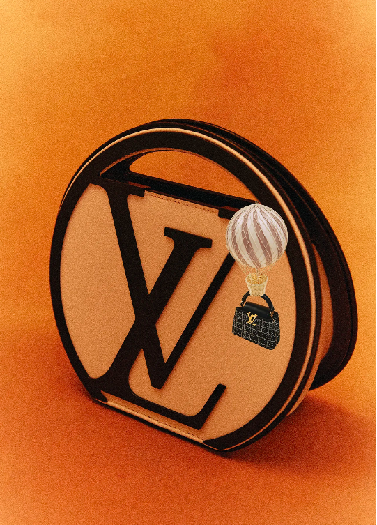 Louis Vuitton handbag and miniature purse charm against a gradient brown background in a studio product fashion shot.