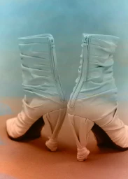 Two light blue heeled boots with zipped backs and sculptural twisted heels shown from behind on a neutral surface