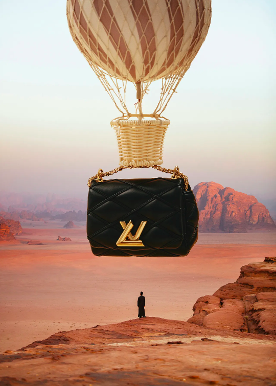 Black Louis Vuitton purse hanging from a hot air balloon over a desert landscape, with a person on a rock formation below.
