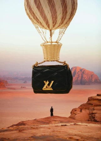 Black Louis Vuitton purse hanging from a hot air balloon over a desert landscape, with a person on a rock formation below.