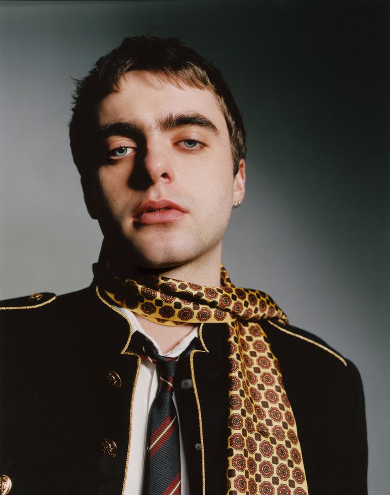 Portrait of Lennon Gallagher wearing a dark military-style jacket and patterned scarf for Behind the Blinds