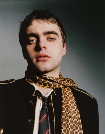 Portrait of Lennon Gallagher wearing a dark military-style jacket and patterned scarf for Behind the Blinds