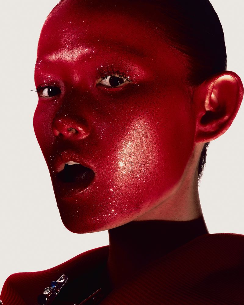 Close-up portrait of a woman with red glitter makeup and her mouth open in a studio, creating a vibrant and expressive visual.