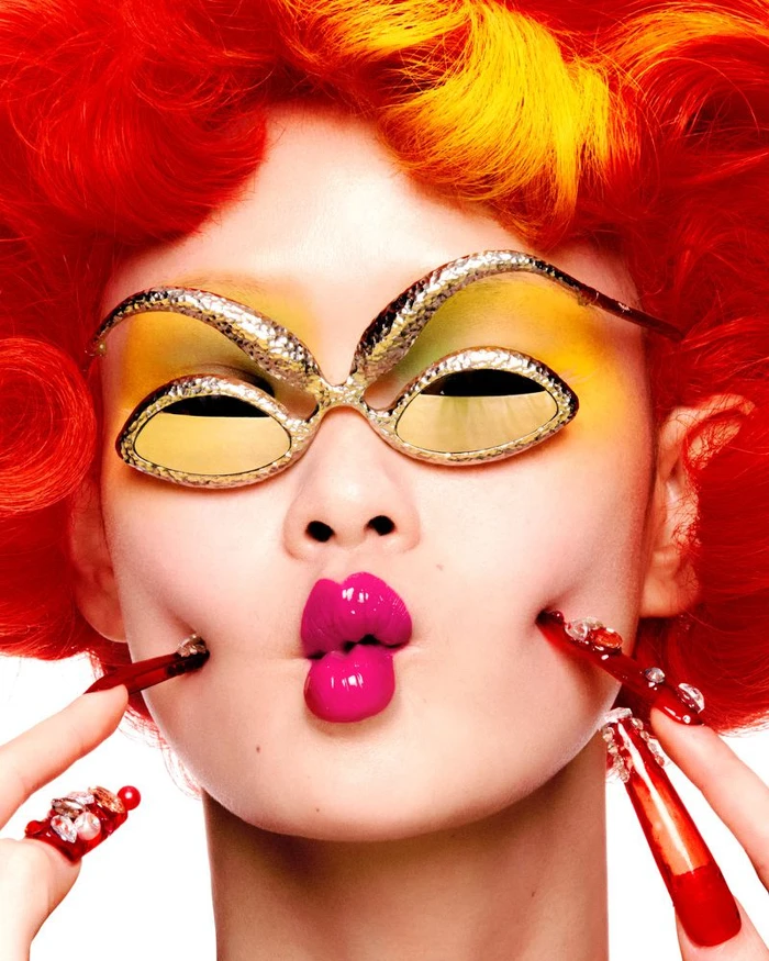Close-up portrait of model with vibrant red hair wearing ornate gold sunglasses and bright pink lipstick for W Magazine China