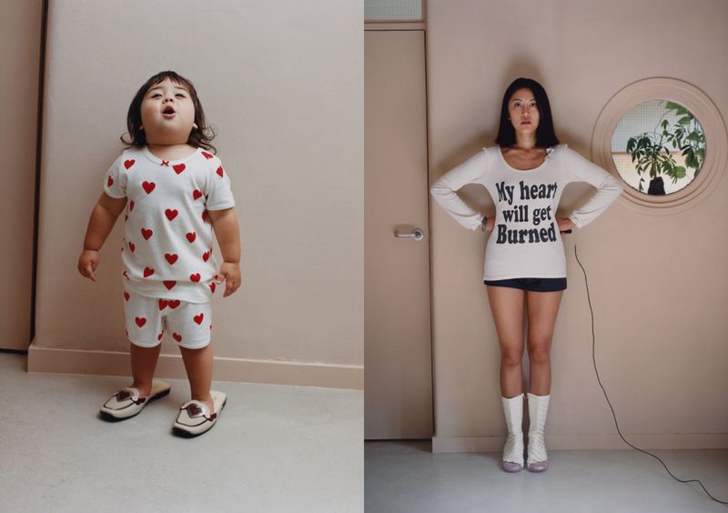 Toddler in heart pajamas and adult woman pose in matching shirts inside a simple peach-colored room under bright, even lighting.