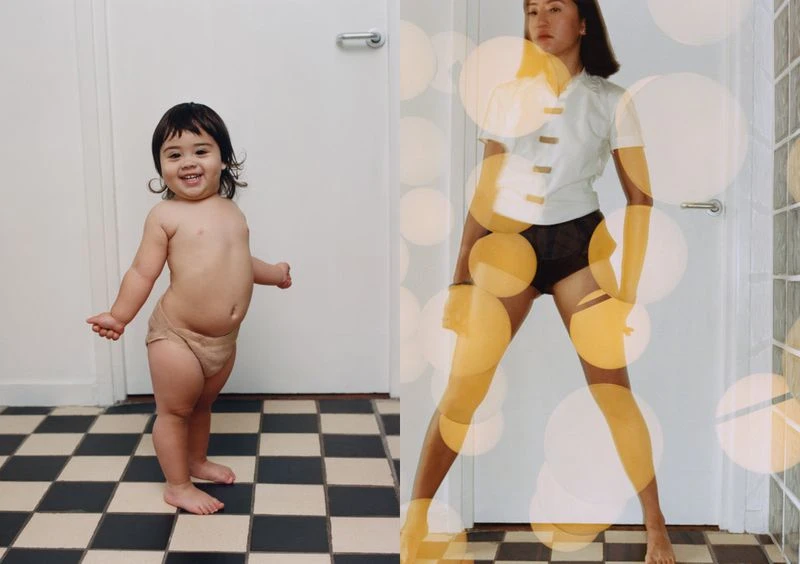 A toddler stands barefoot on a checkered floor next to a woman in shorts, a buttoned shirt, and golden bokeh orbs.