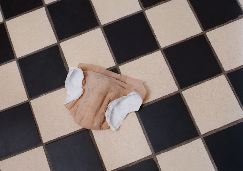 Overhead shot of a wrinkled, tan and white cloth diaper lying on a black and white checkered tile floor, filling the frame.