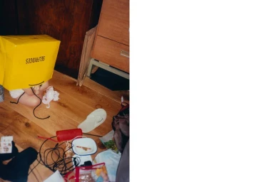 Person with a yellow Selfridges shopping bag over their head sitting on a wooden floor amid scattered personal items.
