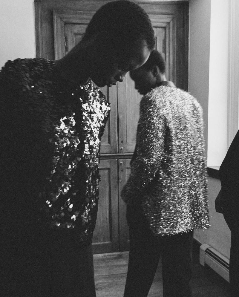 Fashion shoot features two Black models in shimmering jackets in a monochromatic setting, emphasizing texture and style for editorial content.