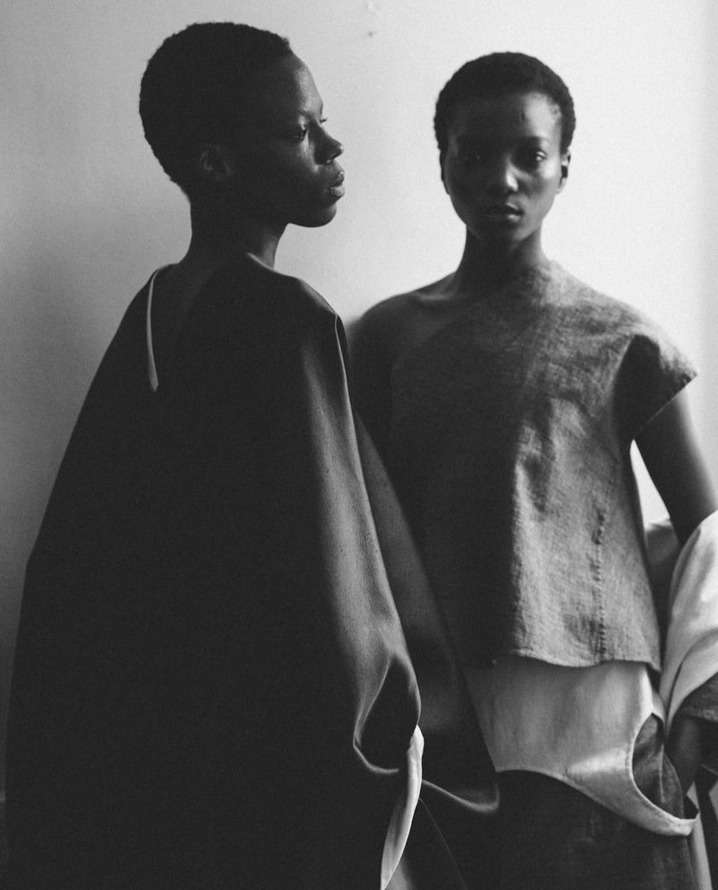 Black and white portrait of two young women with short hair, wearing loose fitting tops, posing in front of a plain background.