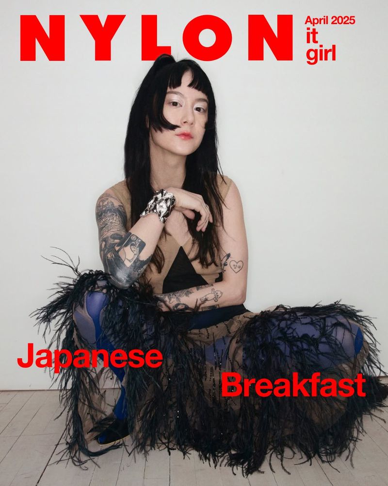 Nylon magazine cover featuring an East Asian woman with black hair and tattoos, seated in a feathered skirt against a white backdrop.
