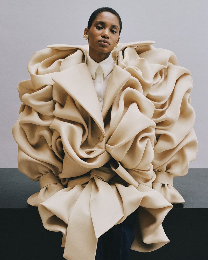 Fashionable woman in a striking, oversized cream-colored coat posing against a neutral background, showcasing its unique design.