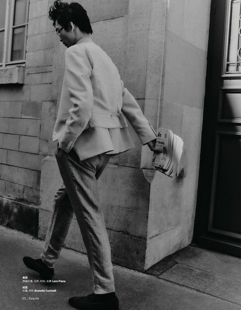 Stylish man walks in light suit, carrying newspaper. Classic fashion, neutral tones, architectural backdrop, and editorial aesthetic.