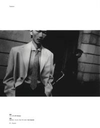 Black and white editorial fashion portrait of a man in a tailored blazer and tie standing on a city street.