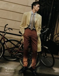 Man wearing a yellow overcoat and brown trousers standing outdoors next to parked bicycles