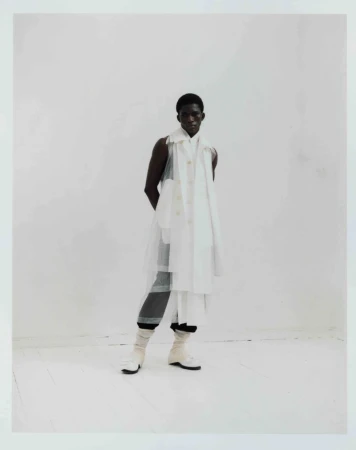 Full-length portrait of a Black male fashion model in a white layered outfit against a white backdrop in a studio setting, stylish and posed.