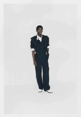 Full-length portrait of a male model wearing dark attire against a plain white studio background.