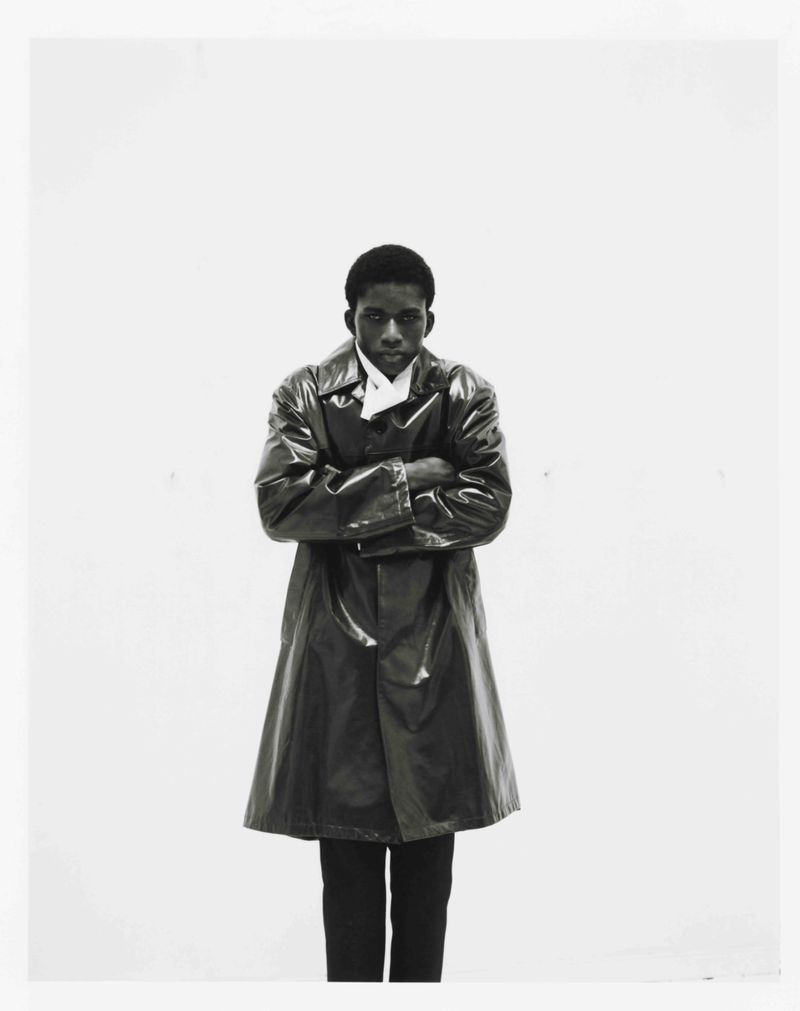 Model Mohammed Banze wearing a glossy dark coat with arms crossed against a white background for The Greatest Magazine.