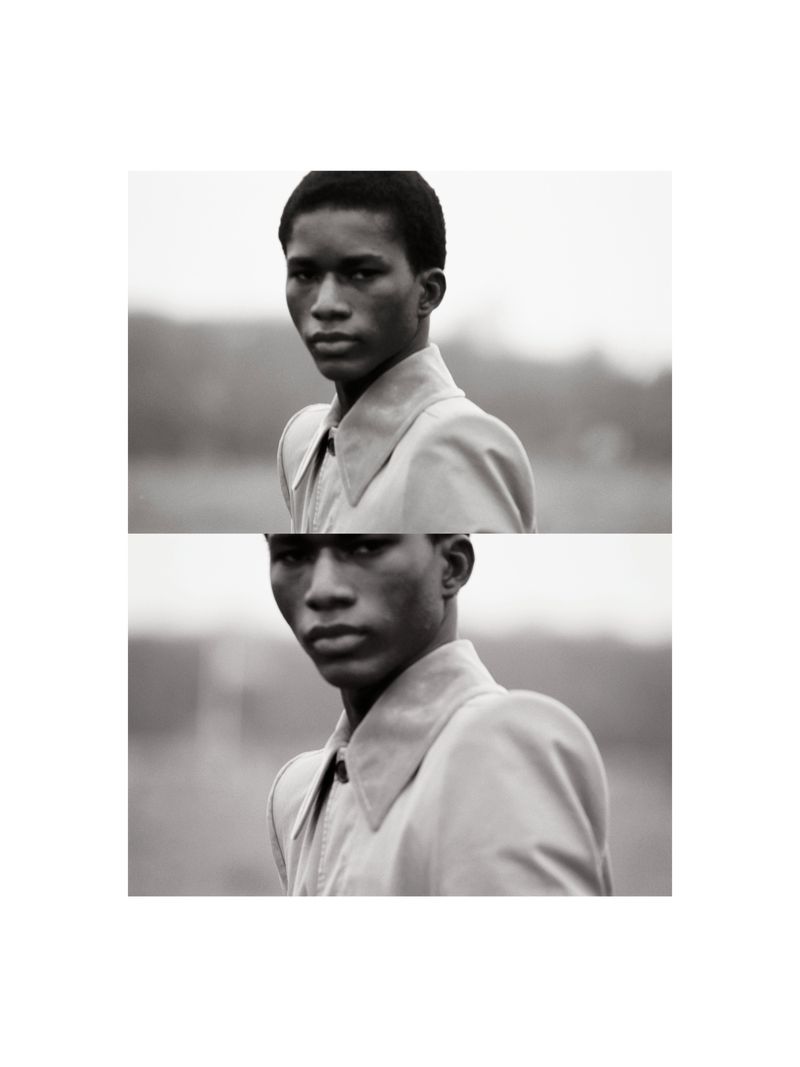 Monochrome portrait of an African-American adult male in a collared jacket, gazing at the camera with a neutral expression outdoors.