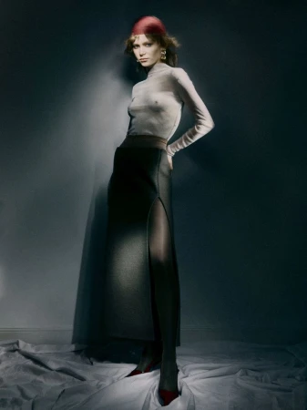 Model Katrina Skudra wearing a sheer turtleneck top and a long black skirt with a high slit for Narcisse Magazine.