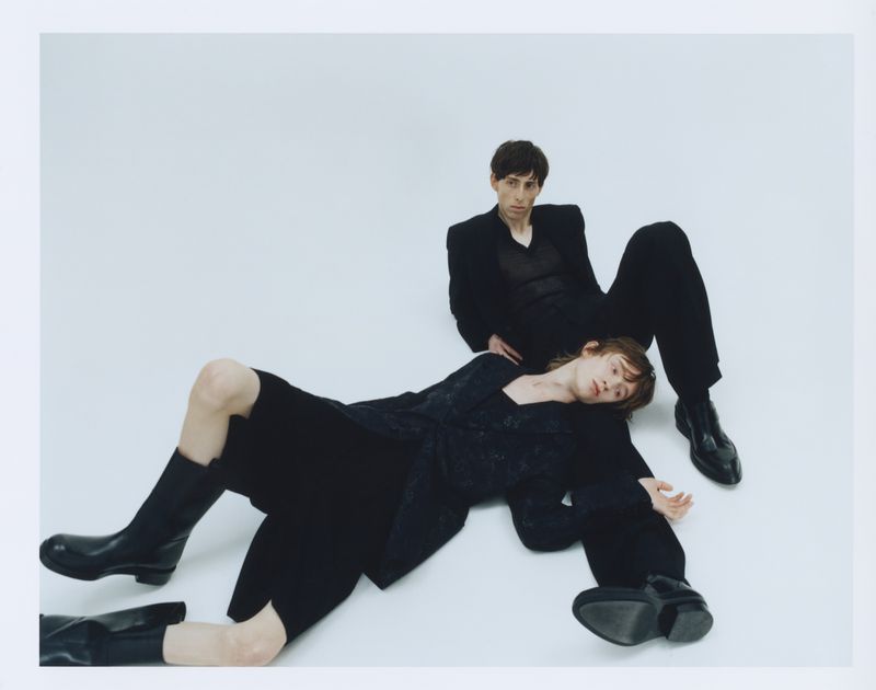 Two models wearing dark clothing posing against a plain white background in a fashion editorial for The Greatest Magazine.