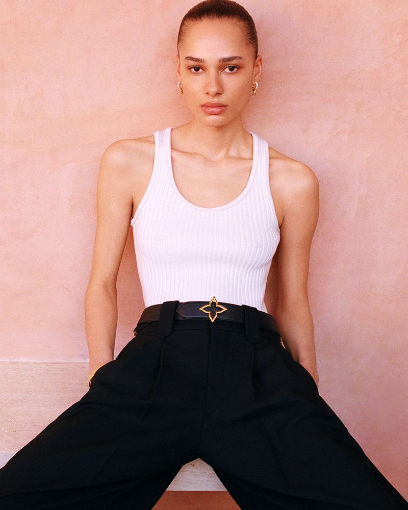 Fashion shot of a woman in a white top and black pants posing in front of a pink background, showcasing a modern and chic style.