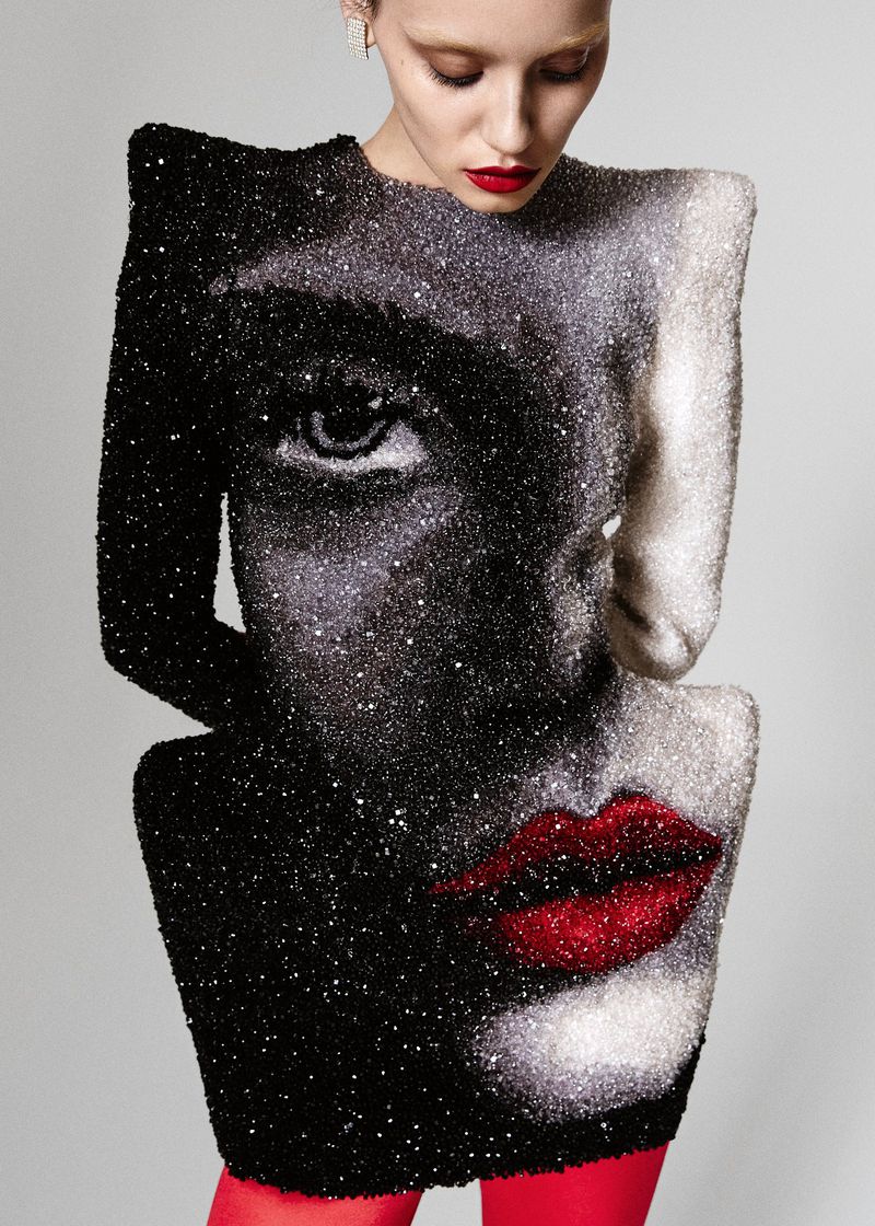 Adult female model wearing black and white dress with a face design, red lipstick, and red tights in a studio setting.