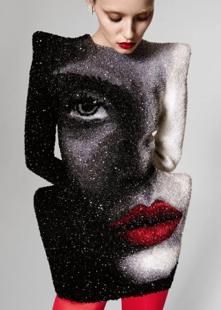 Adult female model wearing black and white dress with a face design, red lipstick, and red tights in a studio setting.