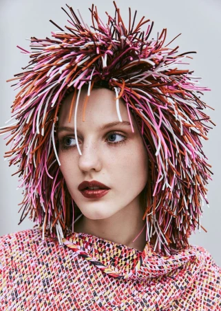 Portrait of a female model wearing a multicoloured woven top and a vibrant, spiky headpiece with white background in studio lighting.