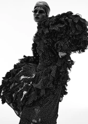 Model in voluminous black polka dot dress, head wrap, and narrow sunglasses against a white background