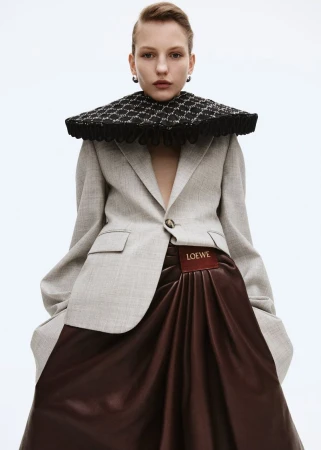 Model wearing a grey blazer, large structured black collar, and brown skirt against a white seamless background